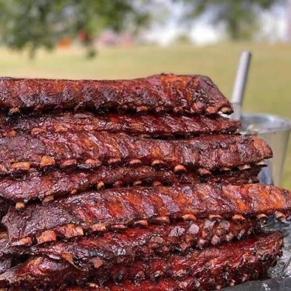 Stack of smoked, glazed baby back ribs served outdoors.